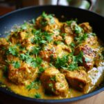 A close-up of a pan filled with creamy coconut chicken curry, garnished with fresh cilantro.