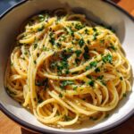 A close-up of a bowl filled with creamy garlic pasta, garnished with fresh parsley and red pepper flakes.