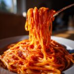 A fork lifting a generous portion of creamy garlic tomato pasta from a white plate.