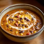 A close-up of a bowl of Creamy Taco Soup, featuring beans, corn, ground meat, and a swirl of cream and cheese.