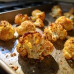 Close-up of golden brown, crispy baked cauliflower florets seasoned with herbs on a baking sheet.