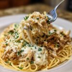 A fork lifting a generous portion of Crock Pot Angel Chicken with creamy sauce and shredded cheese over spaghetti.