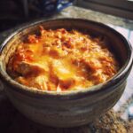 Close-up of a rustic bowl filled with melted cheddar cheese over shredded chicken for crockpot buffalo chicken dip.