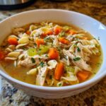 A bowl of steaming Crockpot chicken noodle soup with shredded chicken, carrots, celery, and noodles.