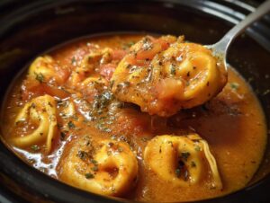 A close-up view of hearty crockpot tomato tortellini soup with a spoonful being lifted.