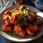 A plate of glistening, crispy Dragon Chicken pieces coated in a rich, spicy sauce, garnished with green onions and sesame seeds.