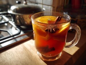 A clear mug filled with warm Dutch oven apple cider, garnished with orange slices, cinnamon sticks, and star anise.