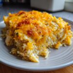 A close-up of a serving of Forgotten Chicken and Rice casserole, topped with melted golden cheese and herbs.