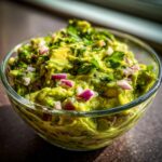 Close-up of a vibrant bowl of fresh guacamole, topped with red onion and cilantro.