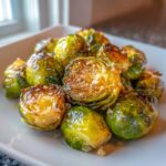 A close-up of glossy, golden-brown garlic butter roasted brussels sprouts piled high on a white plate.