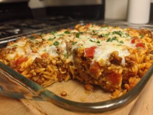 A close-up of a baked ground beef orzo casserole in a glass dish, topped with melted cheese and parsley.