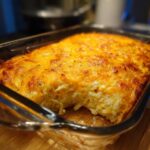 A close-up of a golden-brown hash brown egg casserole baked in a glass dish, with a bite taken out.