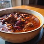 A steaming bowl of hearty crockpot chili with tender beef chunks and kidney beans.