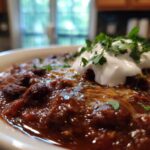 A close-up of a bowl of hearty pumpkin chili topped with sour cream and fresh parsley.