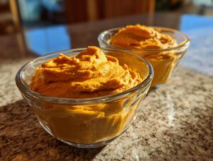 Two glass bowls filled with creamy, vibrant orange high protein pumpkin mousse, ready to be enjoyed.