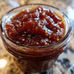Close-up of a jar filled with rich, dark homemade apple butter, showing its thick texture and small seeds.