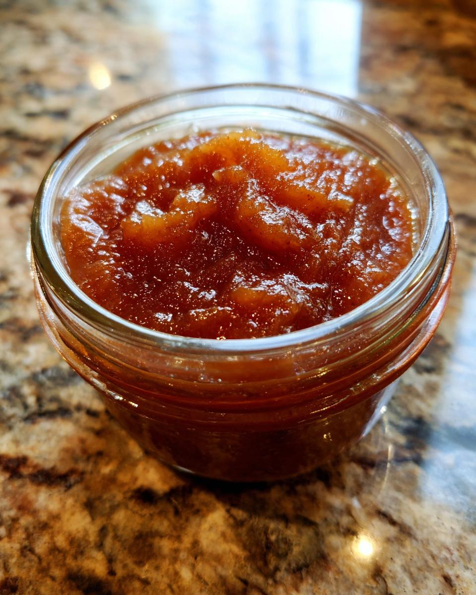 A close-up of a glass jar filled with rich, homemade apple butter.