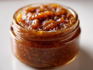 Close-up of a small glass jar filled with rich, dark homemade apple butter.