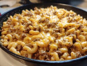 Close-up of delicious homemade hamburger helper with elbow macaroni and melted cheese in a cast iron skillet.