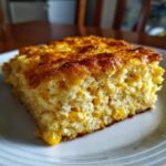 A close-up, mouth-watering slice of jiffy corn casserole on a white plate, showcasing whole corn kernels within the fluffy texture.