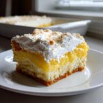 A delicious slice of lemon cream cheese dump cake with a fluffy white topping and a bright yellow filling.