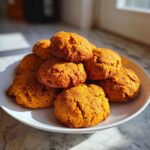 A stack of golden-brown maple pumpkin cookies dusted with sugar on a white plate.
