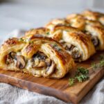 A close-up of a golden-brown mushroom gruyere puff pastry braid, sliced to reveal a savory mushroom and cheese filling.