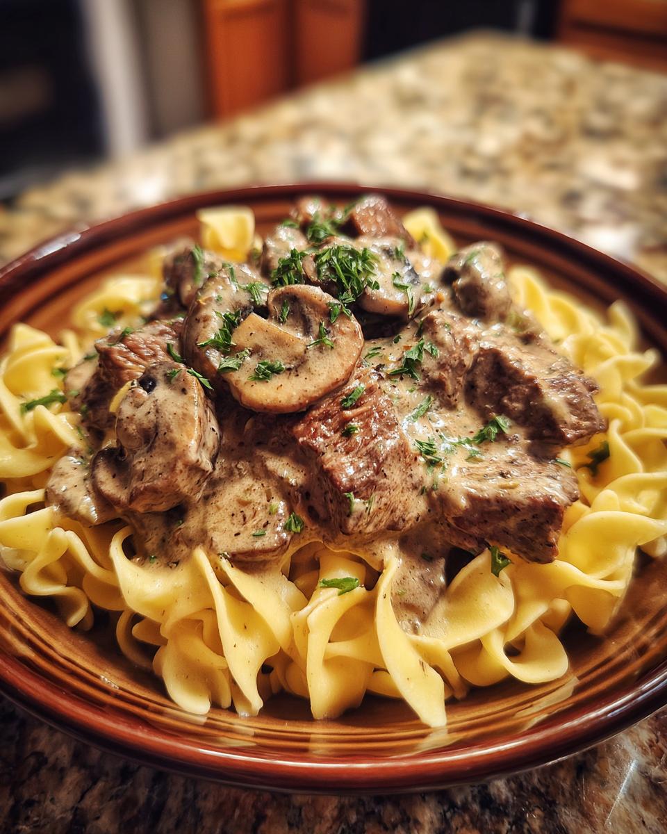 A close-up of old fashioned beef stroganoff served over egg noodles, topped with mushrooms and parsley.