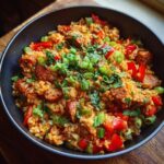 A close-up view of a hearty bowl of one pan jambalaya, filled with rice, sausage, chicken, bell peppers, and garnished with green onions and parsley.