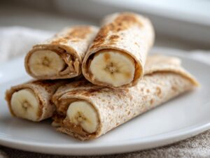 Close-up of peanut butter banana roll-ups on a white plate, showcasing whole banana slices and creamy peanut butter.