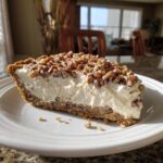 A slice of decadent pecan cream pie on a white plate, showcasing a creamy filling and pecan topping.