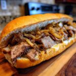 A close-up view of a delicious Philly cheesesteak sandwich filled with thinly sliced steak, melted cheese, and caramelized onions on a toasted roll.
