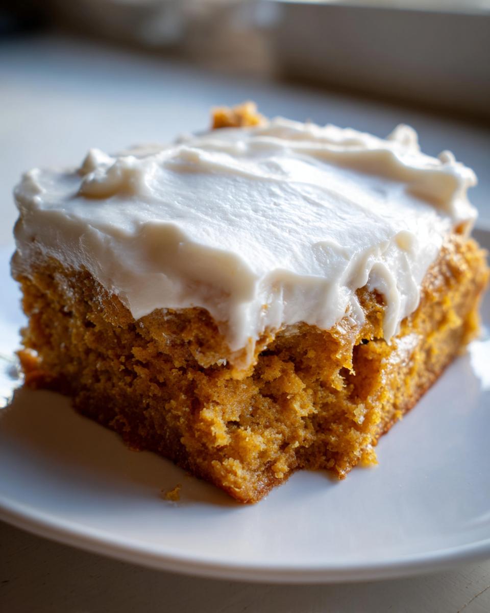 A delicious slice of pumpkin bars with thick cream cheese frosting on a white plate.