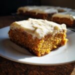 A slice of pumpkin bars with creamy frosting on a white plate, showing the texture of the bar and frosting.