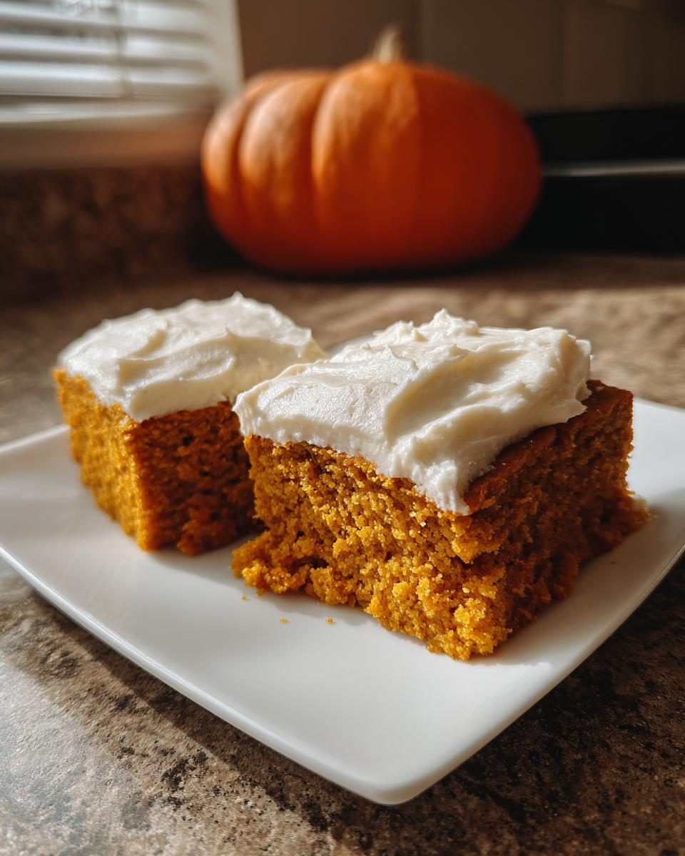 Two delicious pumpkin bars with creamy frosting piled high on a white plate, with a whole pumpkin in the background.