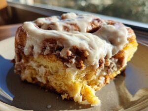 Close-up of a fluffy pumpkin cinnamon roll generously topped with cream cheese frosting.