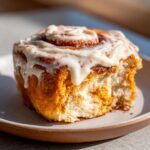 Close-up of a delicious pumpkin cinnamon roll with creamy frosting and a bite taken out.