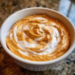 Close-up of a white bowl filled with creamy pumpkin dip swirled with Cool Whip.