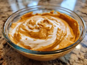 A close-up of creamy pumpkin dip swirled with Cool Whip in a glass bowl.