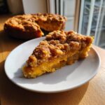 A close-up of a slice of pumpkin dump cake on a white plate, with the rest of the cake in the background.