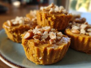 Close-up of several Pumpkin Protein Cups topped with chopped nuts on a light blue plate.