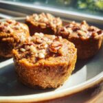 Close-up of four Pumpkin Protein Cups topped with chopped pecans, arranged on a plate.