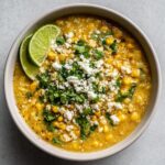 A bowl of creamy Slow Cooker Mexican Street Corn Soup topped with crumbled cotija cheese, fresh cilantro, and lime wedges.