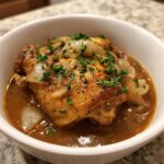 A close-up of a piece of southern smothered chicken in a rich brown gravy with onions and parsley.