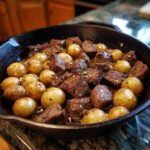 A close-up of juicy steak bites and golden baby potatoes cooked in a cast iron skillet.