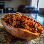 A baked sweet potato, split open and filled with hearty, savory sweet potato sloppy joes mixture.