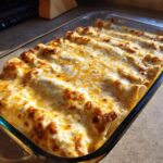 A close-up of a baking dish filled with golden-brown, cheesy white chicken enchiladas.