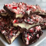 Stack of broken pieces of homemade peppermint bark showing dark chocolate, white chocolate layer, and crushed candy canes.