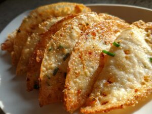 Close-up of golden-brown, crispy air fryer rice paper dumplings arranged on a white plate, garnished with green onions.
