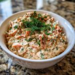 A creamy, pinkish salmon dip topped generously with fresh dill, served in a white bowl.